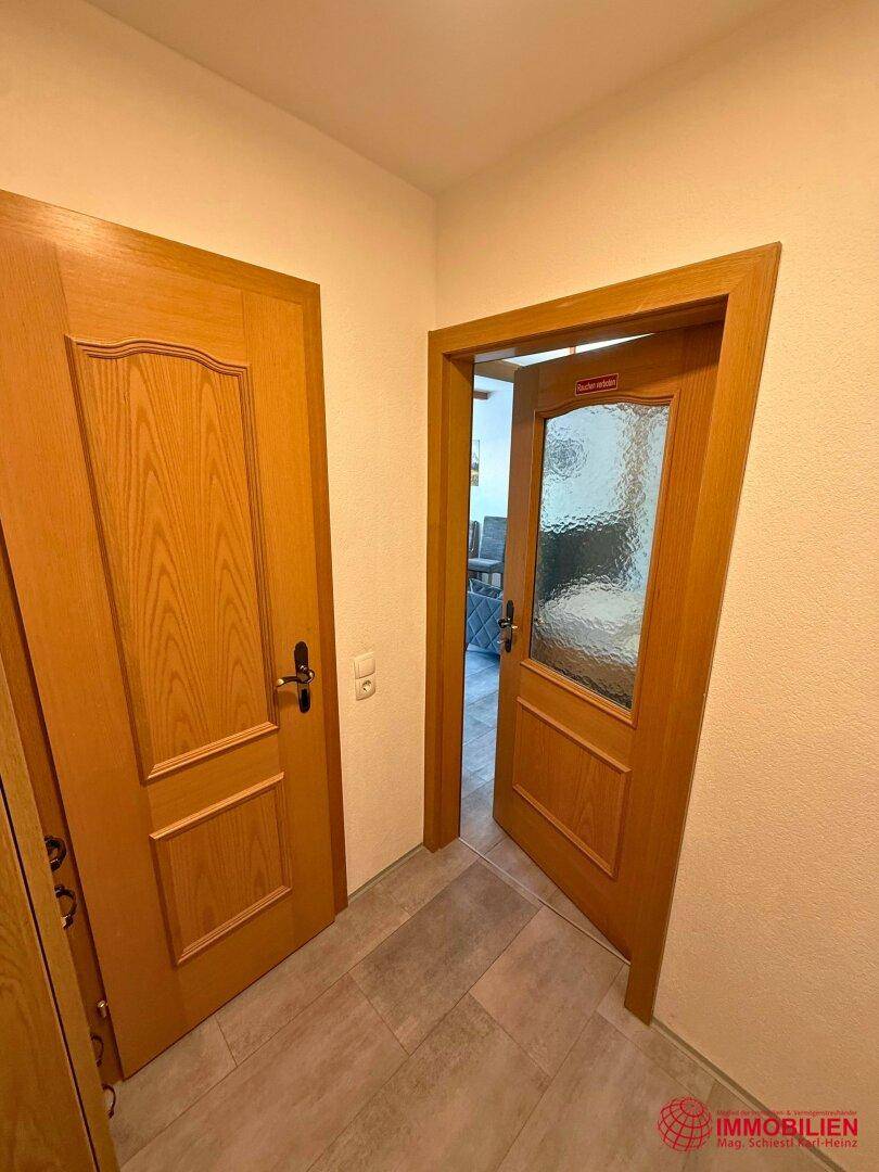 Heller Flur mit zwei Holztüren und modernem Fliesenboden.