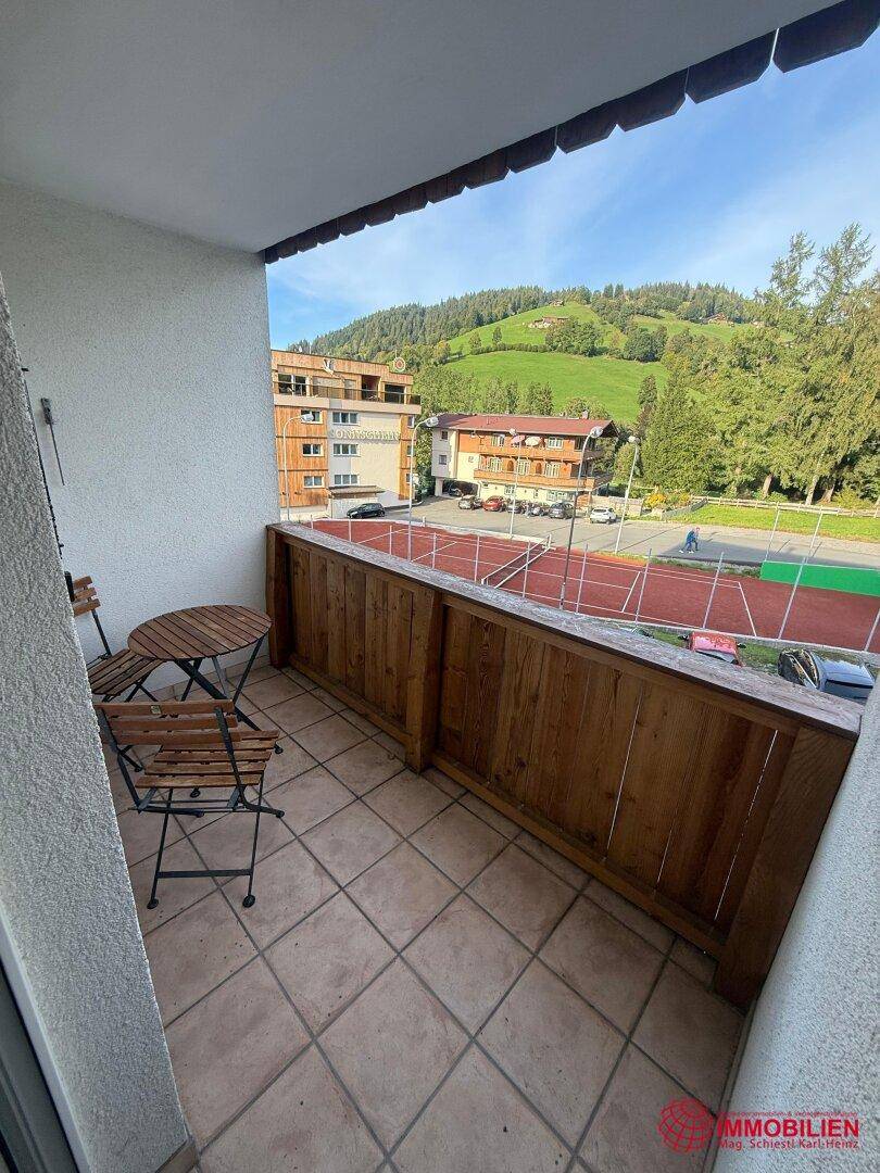 Balkon mit Holzbodenfliesen und Blick auf einen Tennisplatz und grüne Hügel.