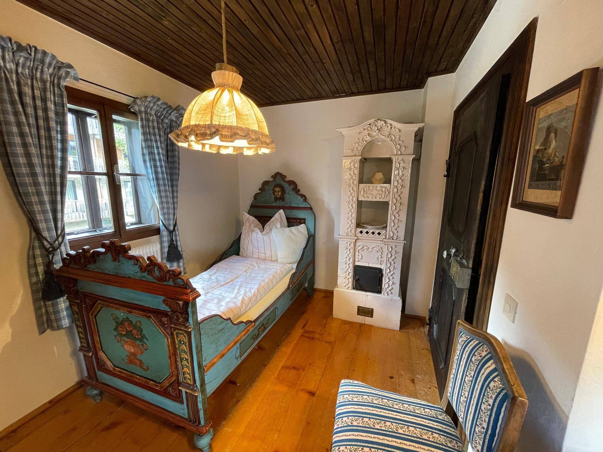 Gemütliches Schlafzimmer mit traditionellem Himmelbett, Kachelofen und Holzbalkendecke.