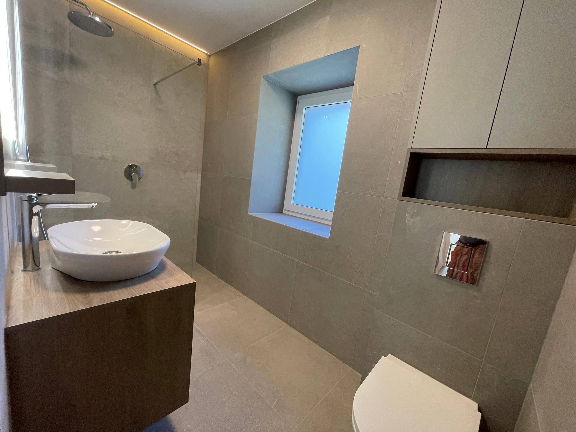 Modernes Badezimmer mit grauen Fliesen, schwebendem Waschtisch, Wand-WC und begehbarer Dusche.