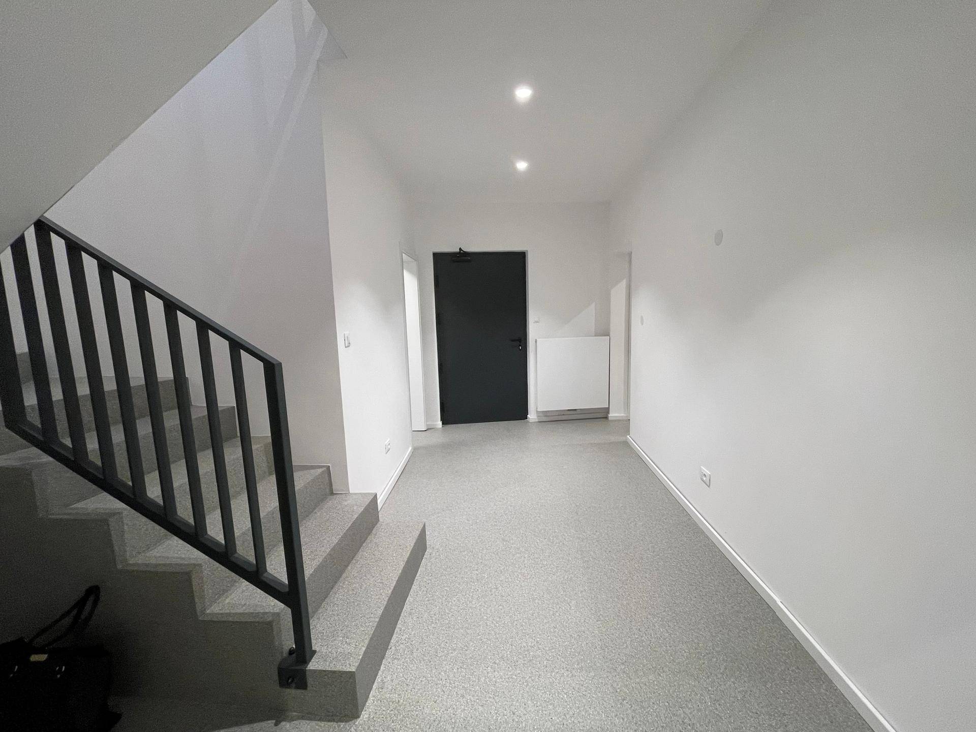 Heller Flur mit Treppenaufgang und moderner Eingangstür, ausgestattet mit Einbaustrahlern.