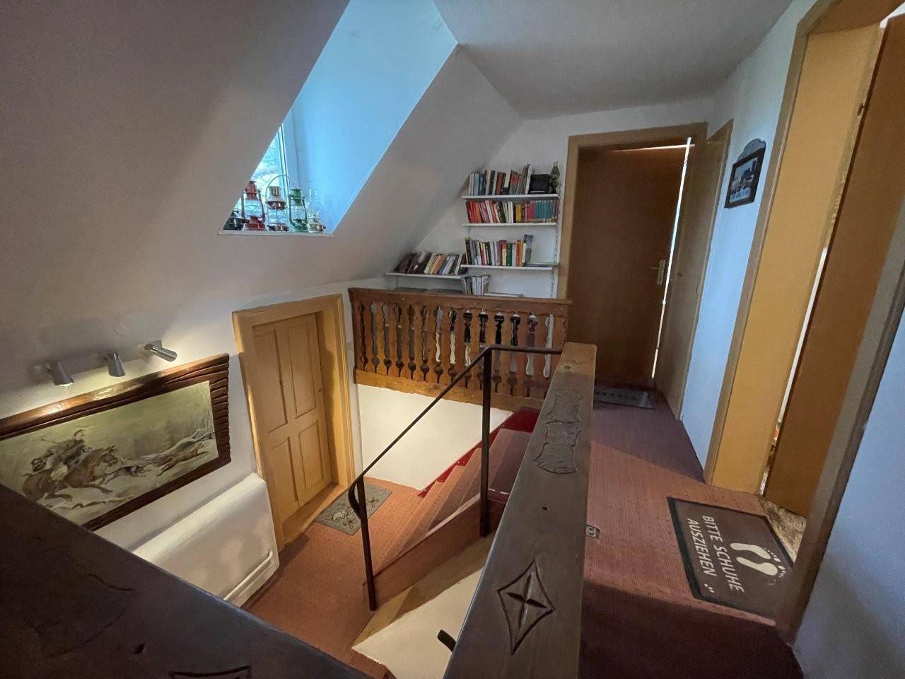 Rustikaler Treppenaufgang mit Holzgeländer und Dachschräge, der zu den oberen Etagen führt.