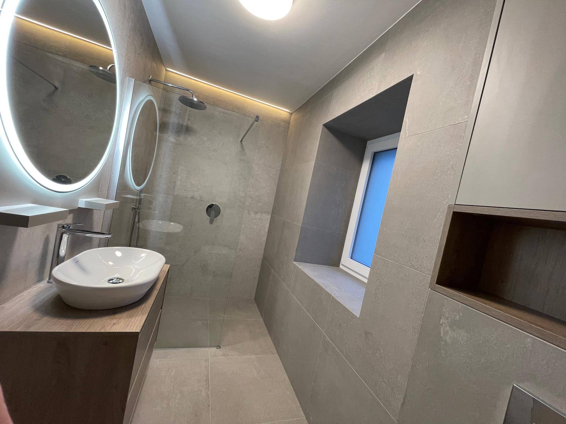 Elegantes Badezimmer mit großer begehbarer Dusche, Waschtisch und Fenster für Tageslicht.