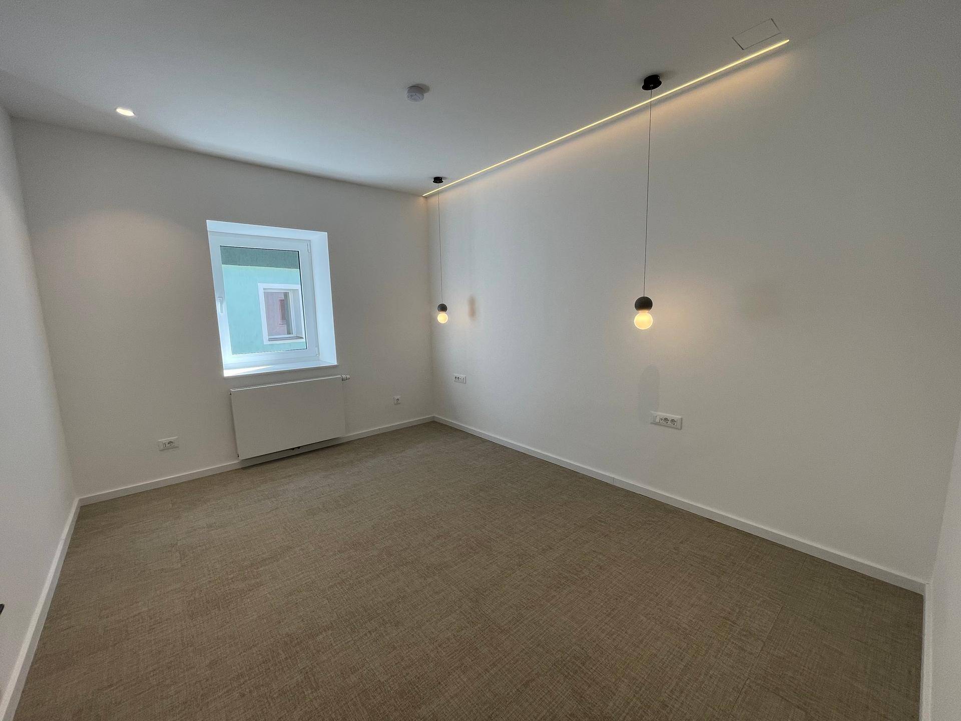 Geräumiges, helles Zimmer mit Teppichboden, modernem Lichtkonzept und einem Fenster.