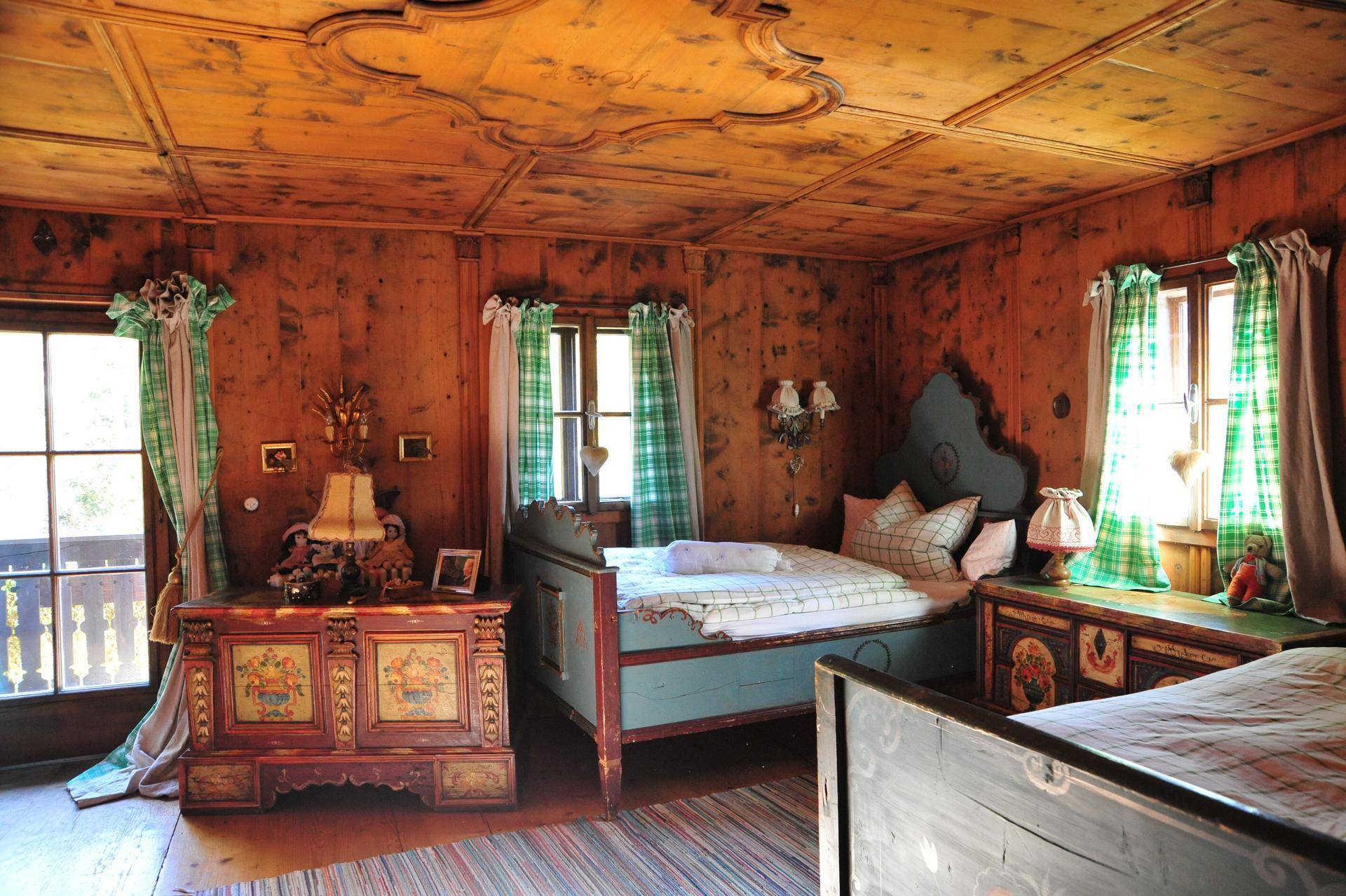 Rustikales Schlafzimmer im Alpenstil mit holzvertäfelten Wänden, Decke und bemalten Möbeln.