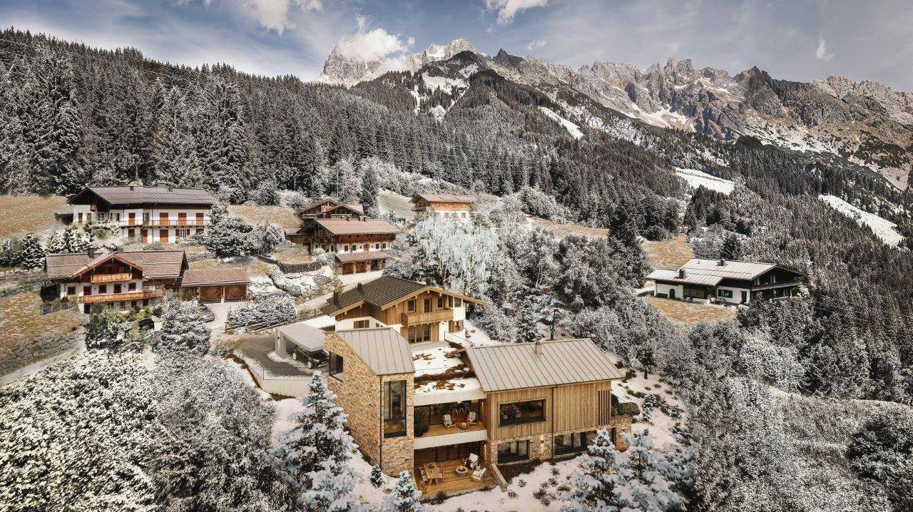 Luftaufnahme eines modernen Chalet-Komplexes eingebettet in eine verschneite Berglandschaft mit Wald.