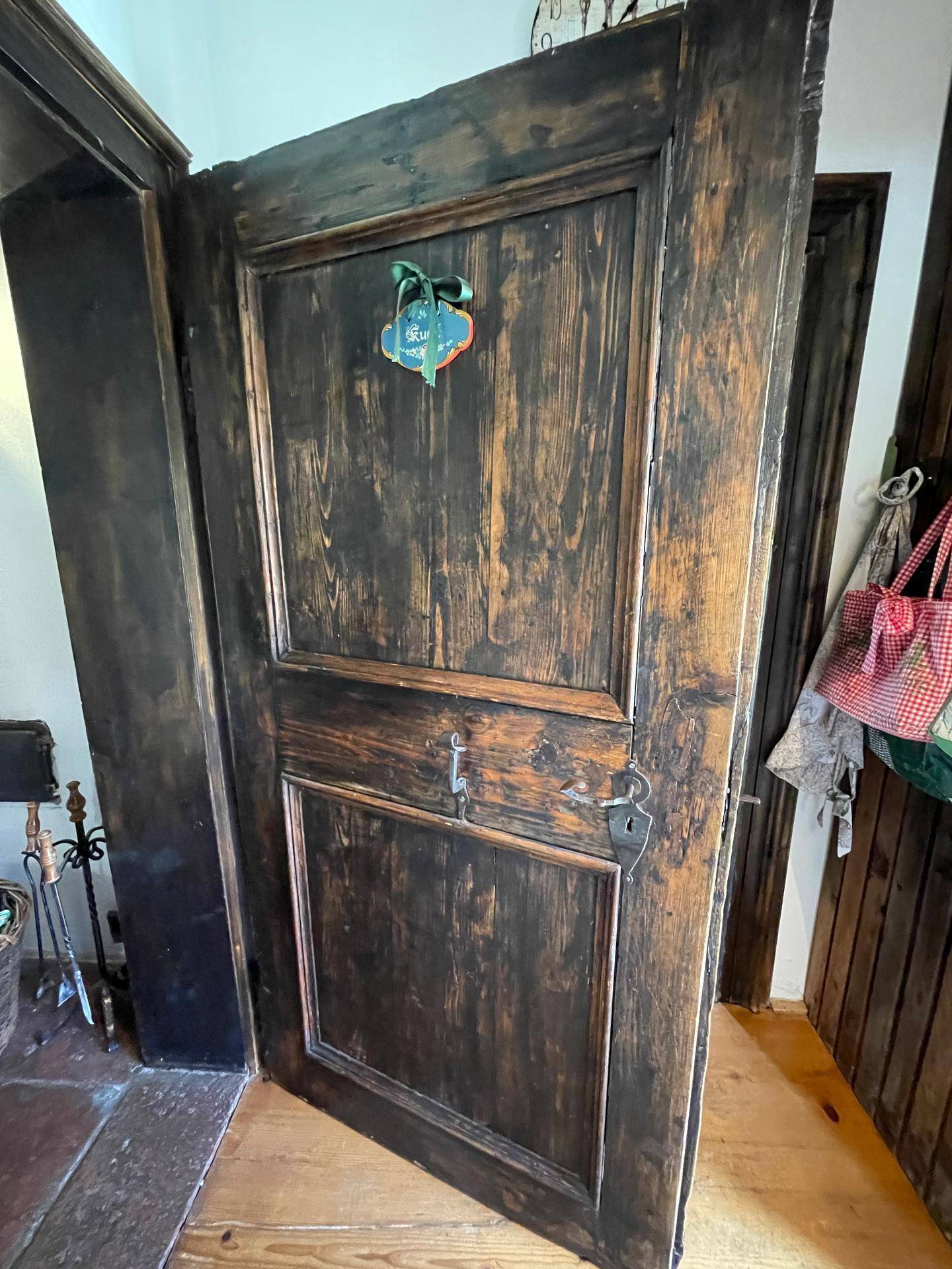 Rustikale Holztür mit dunkler Patina und traditionellen Beschlägen in einem Innenraum.