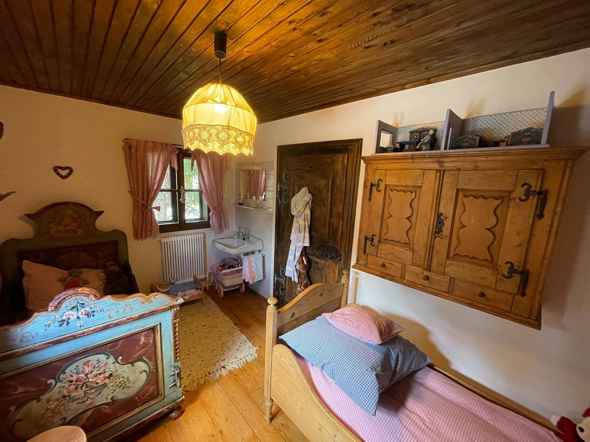 Helles Schlafzimmer mit zwei Betten, Holzboden und einem kleinen Waschbecken in der Ecke.