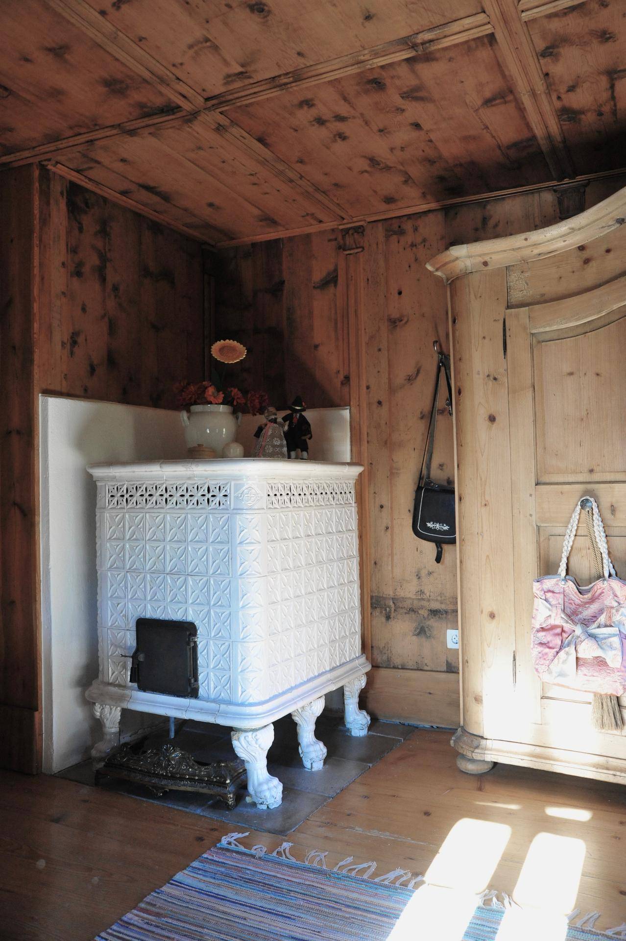 Traditioneller Kachelofen in einem Raum mit holzvertäfelten Wänden und einem Holzschrank.