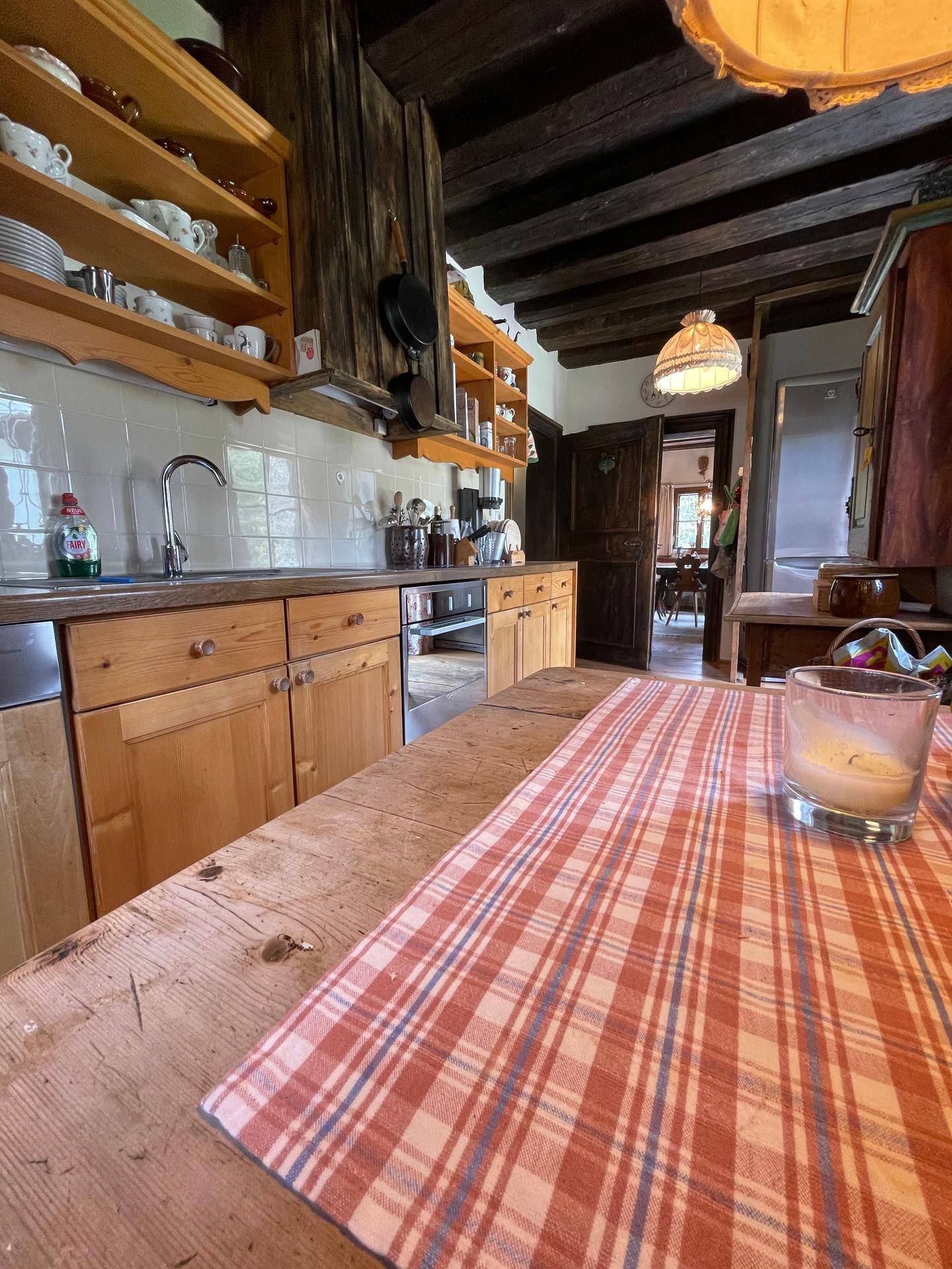 Blick von der Essecke in die traditionelle Holzküche mit Arbeitsplatte und Geräten.