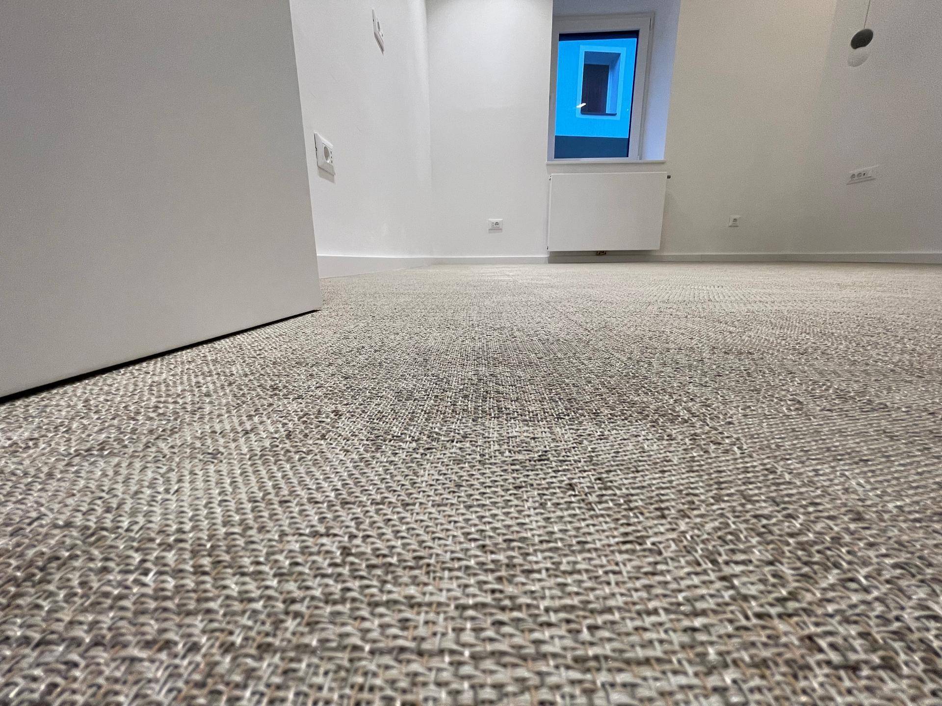 Nahaufnahme eines strukturierten Teppichbodens in einem hellen Raum mit Fenster.