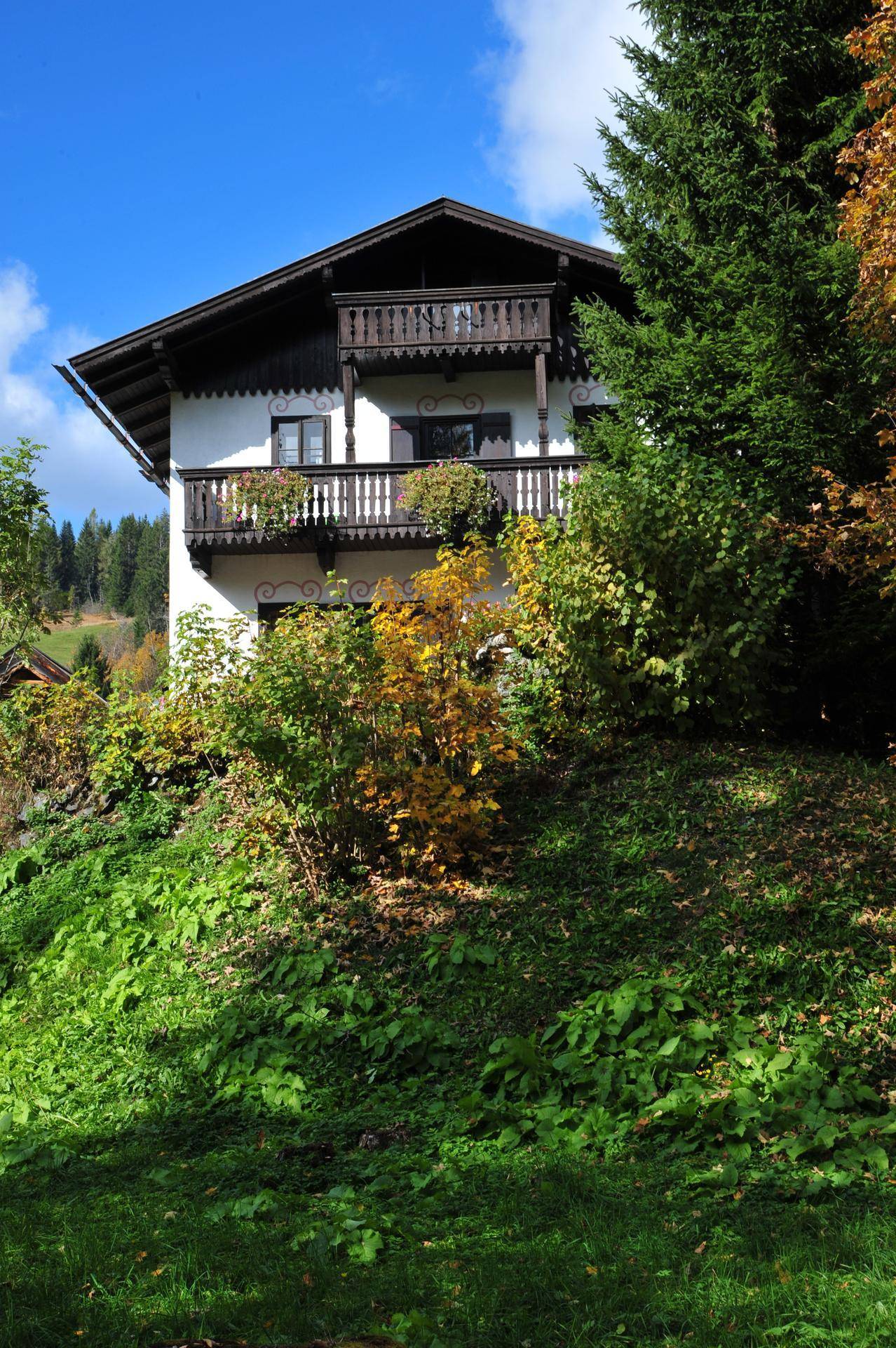 Traditionelles Alpenhaus mit Balkonen und üppiger Vegetation auf einem Hanggrundstück.