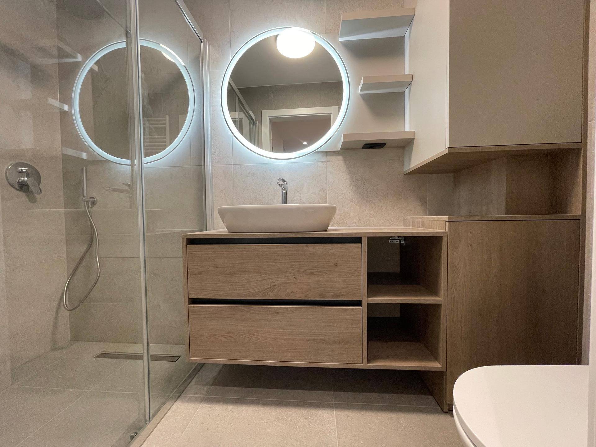 Modernes Badezimmer mit Waschtisch, beleuchtetem Spiegel und ebenerdiger Dusche.