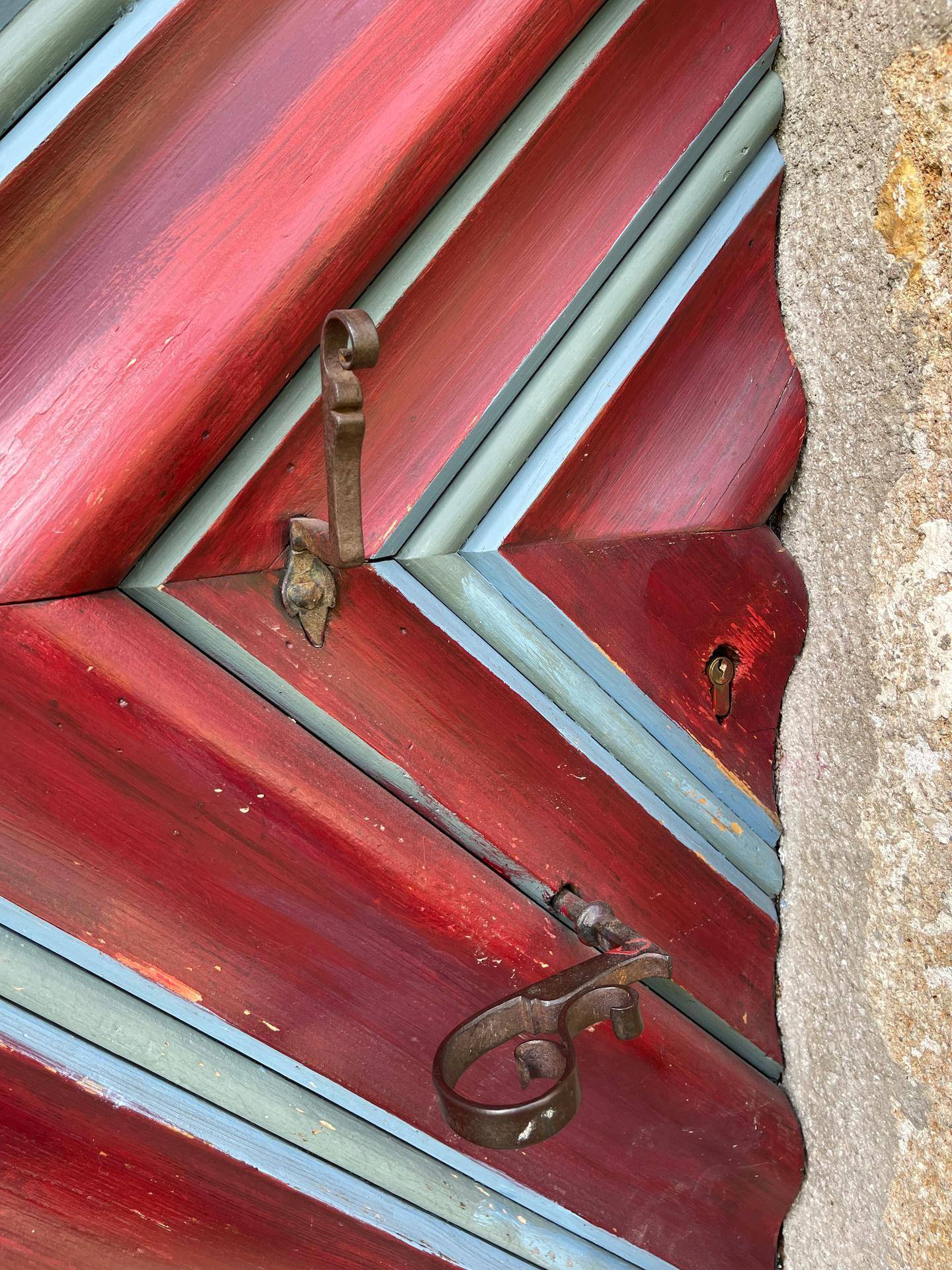 Detailaufnahme einer traditionellen Holztür mit roten und blauen Streifen und rustikalen Beschlägen.