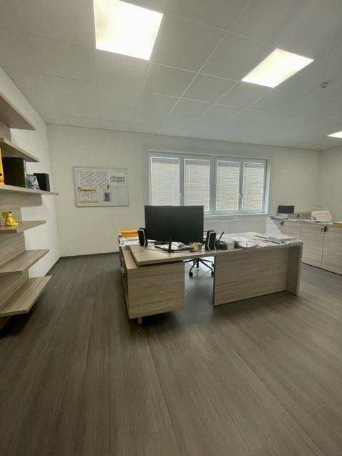 Modernes Büro mit einem Schreibtisch, Computer und Regalen, beleuchtet durch ein Fenster.