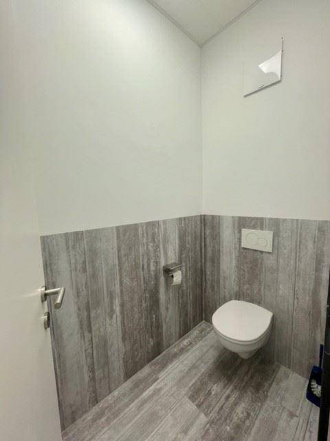 Saubere Toilette mit Wand-WC und Holzoptik-Fliesen, ausgestattet mit einem Abluftventilator.