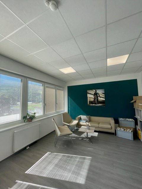 Moderner Büroloungebereich mit einer dunkelblauen Akzentwand, bequemen Sitzgelegenheiten und großen Fenstern.