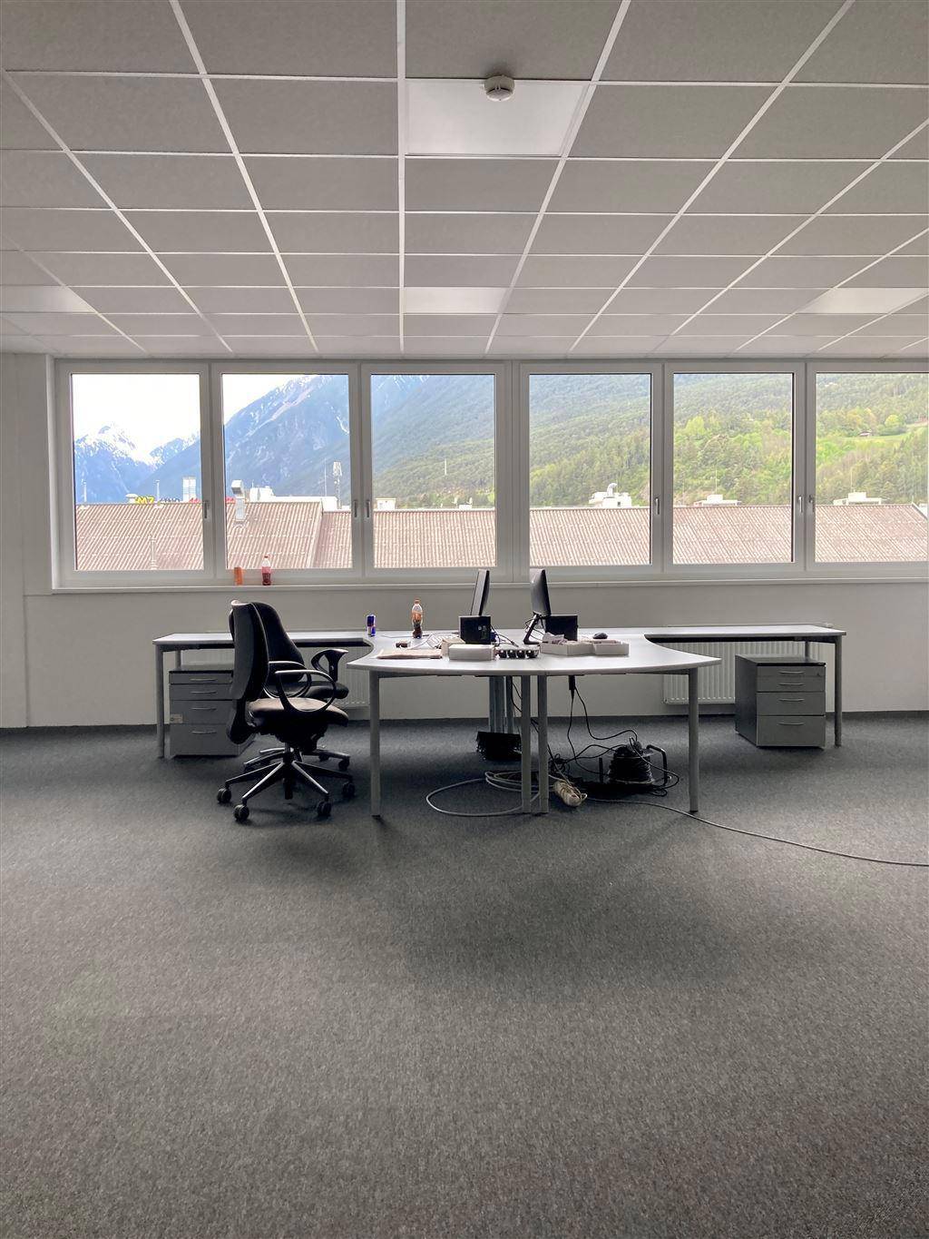 Helles Büro mit großen Fenstern, die einen weiten Bergblick bieten, ausgestattet mit Schreibtischen und Teppichboden.