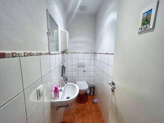 Kleines Gäste-WC mit weißen Fliesen, Terrakotta-Boden und wandhängendem WC sowie einem Spiegel.