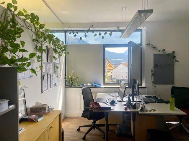 Büro mit Schreibtischen, Computern und einem Fenster, das einen Blick auf die Berge bietet.