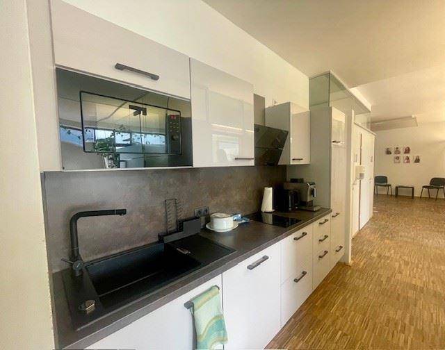 Moderne Küche mit weißen Hochglanzschränken, dunkler Arbeitsplatte und integrierten Geräten.