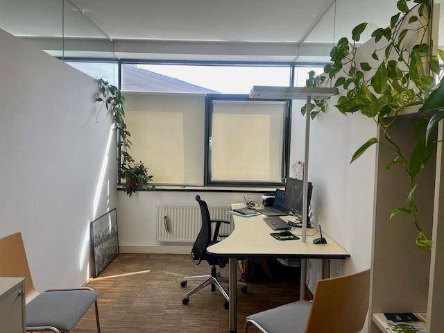 Ruhiges Büro mit Schreibtisch, Stühlen und einem großen Fenster, das viel Tageslicht hereinlässt.