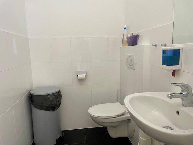 Helles Badezimmer mit weiß gefliesten Wänden, Toilette und einem modernen Waschbecken.