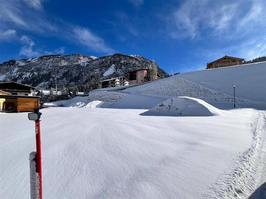Weite, schneebedeckte Fläche mit Bergen und Häusern in der Ferne an einem sonnigen Wintertag.