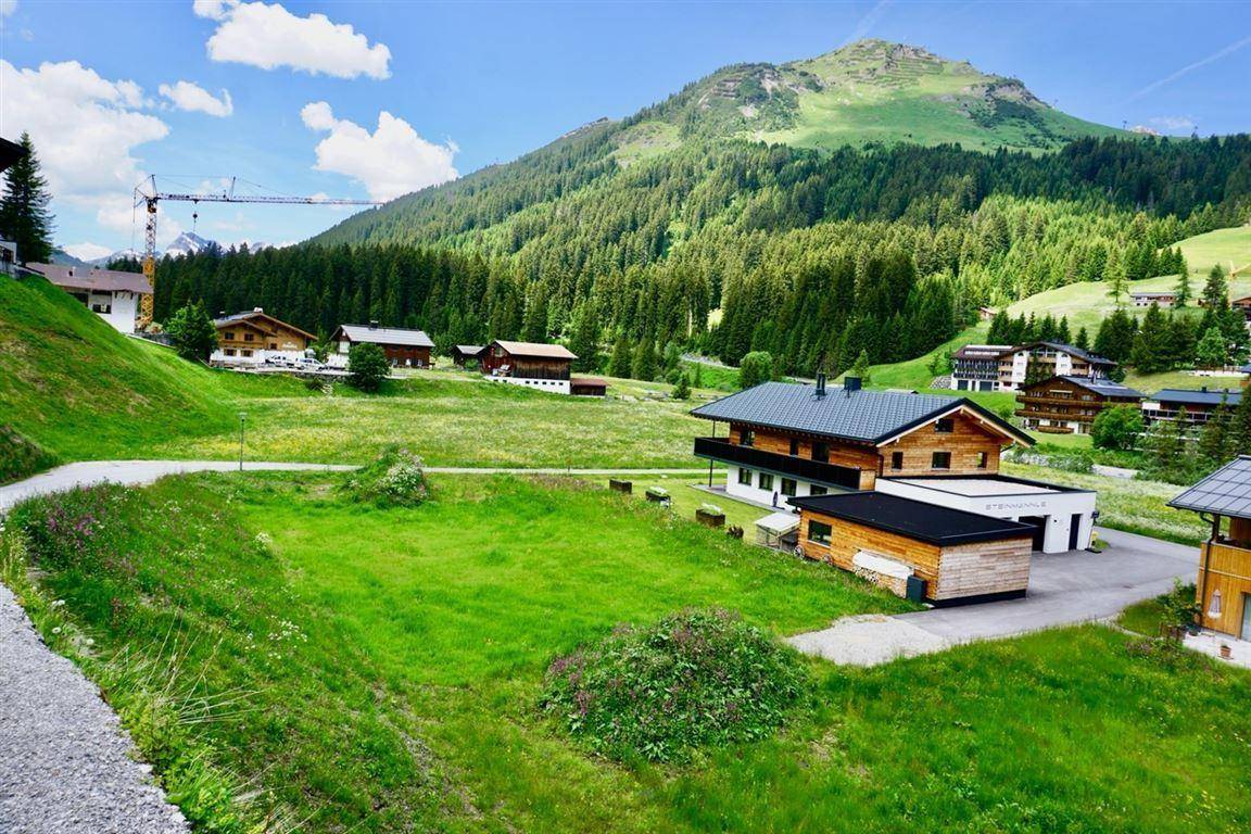 Alpines Wohnhaus mit Holzelementen und Balkon, umgeben von grünen Wiesen und Bergen.