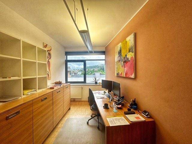 Funktionales Büro mit Schreibtisch, Regalen und einer Akzentwand in warmem Braunton mit Bergblick.