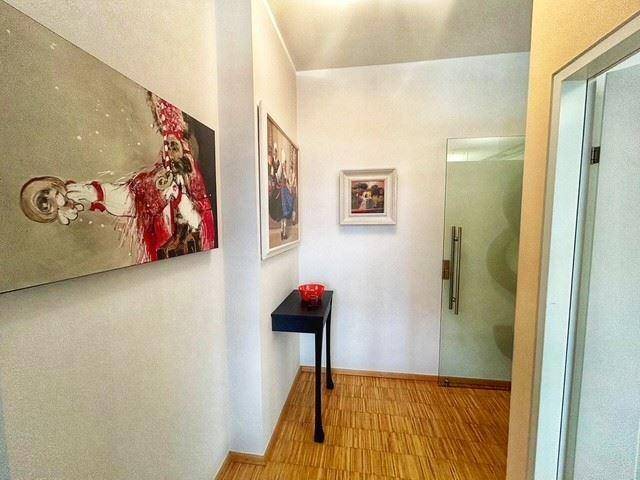 Schmaler Flur mit Holzboden, moderner Kunst an den Wänden und einer Glastür.