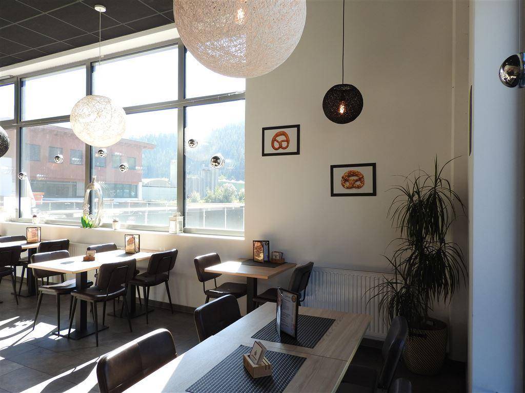 Gemütlicher Sitzbereich in einem Café mit großen Fenstern, Pflanzen und modernen Leuchten.