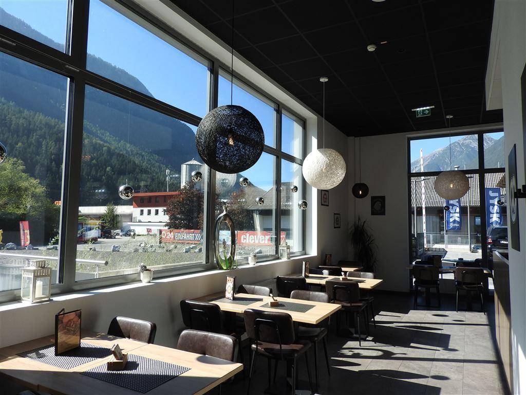 Heller Gastraum mit großen Fenstern, Blick auf die Berge und moderne Hängelampen.