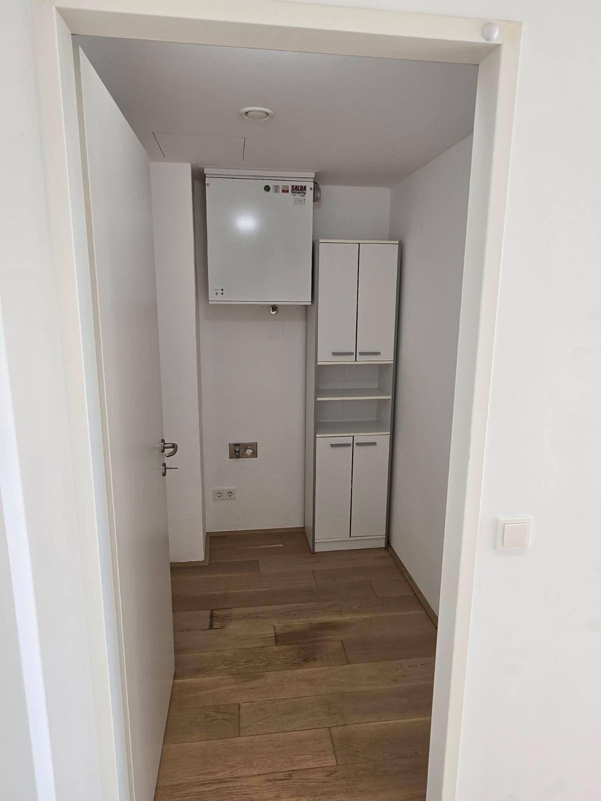 Kleiner Abstellraum mit Holzboden, einem Wandschrank und einem Lüftungssystem an der Decke.