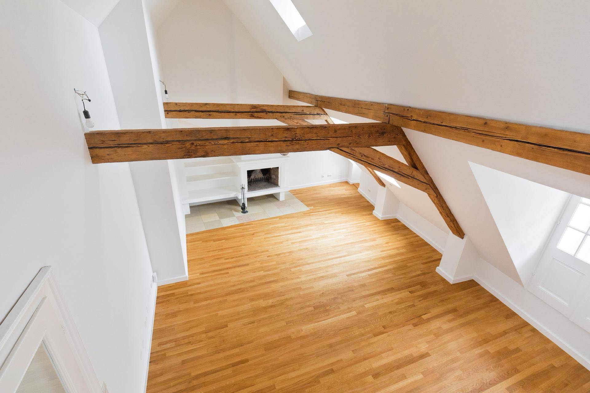 Weitläufiger Dachgeschossraum mit Holzbalken, Parkettboden und Kamin aus der Vogelperspektive.