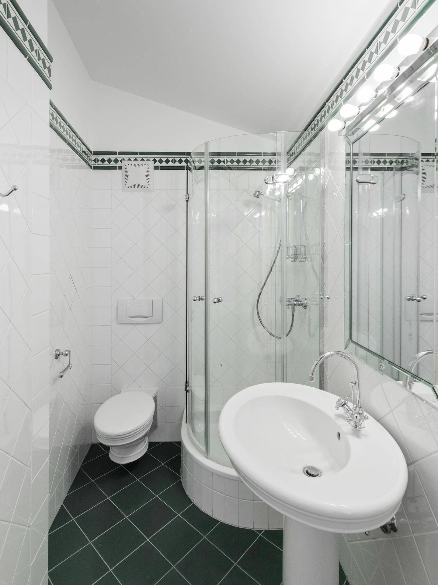 Kleines Badezimmer mit Dusche, WC und grün-weißen Fliesen.