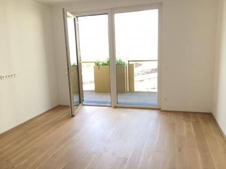 Geräumiges Schlafzimmer mit Holzboden und großen Fenstern, die Zugang zu einem Balkon bieten.