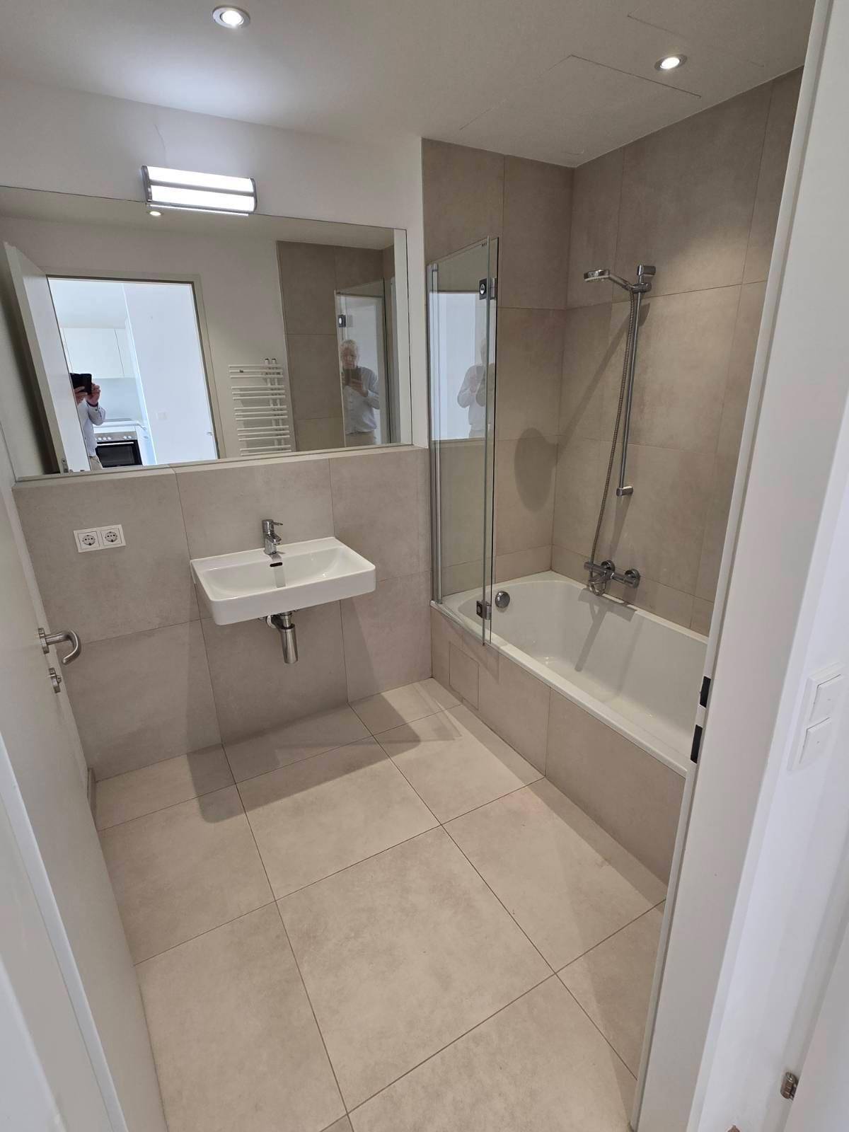 Modernes Badezimmer mit Badewanne, Duschvorrichtung, Waschbecken und großen Fliesen.