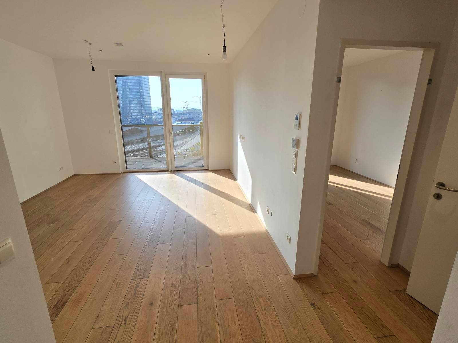 Heller Wohnbereich mit Holzboden und Zugang zu einem Balkon, der viel Tageslicht hereinlässt.