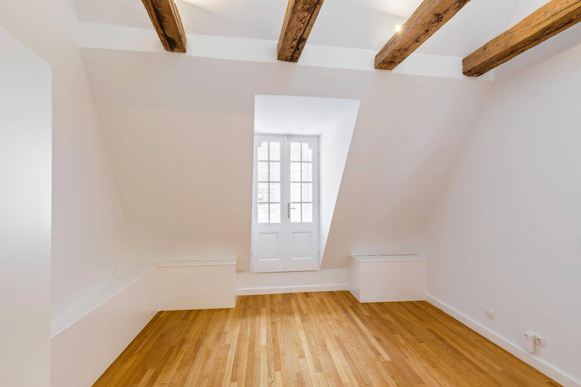 Helles Zimmer im Dachgeschoss mit Holzbalken und französischem Balkon.