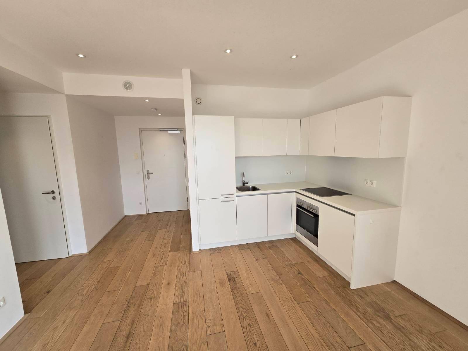 Moderne, offene Küchenzeile mit weißen Schränken und Holzboden in einem hellen Raum.