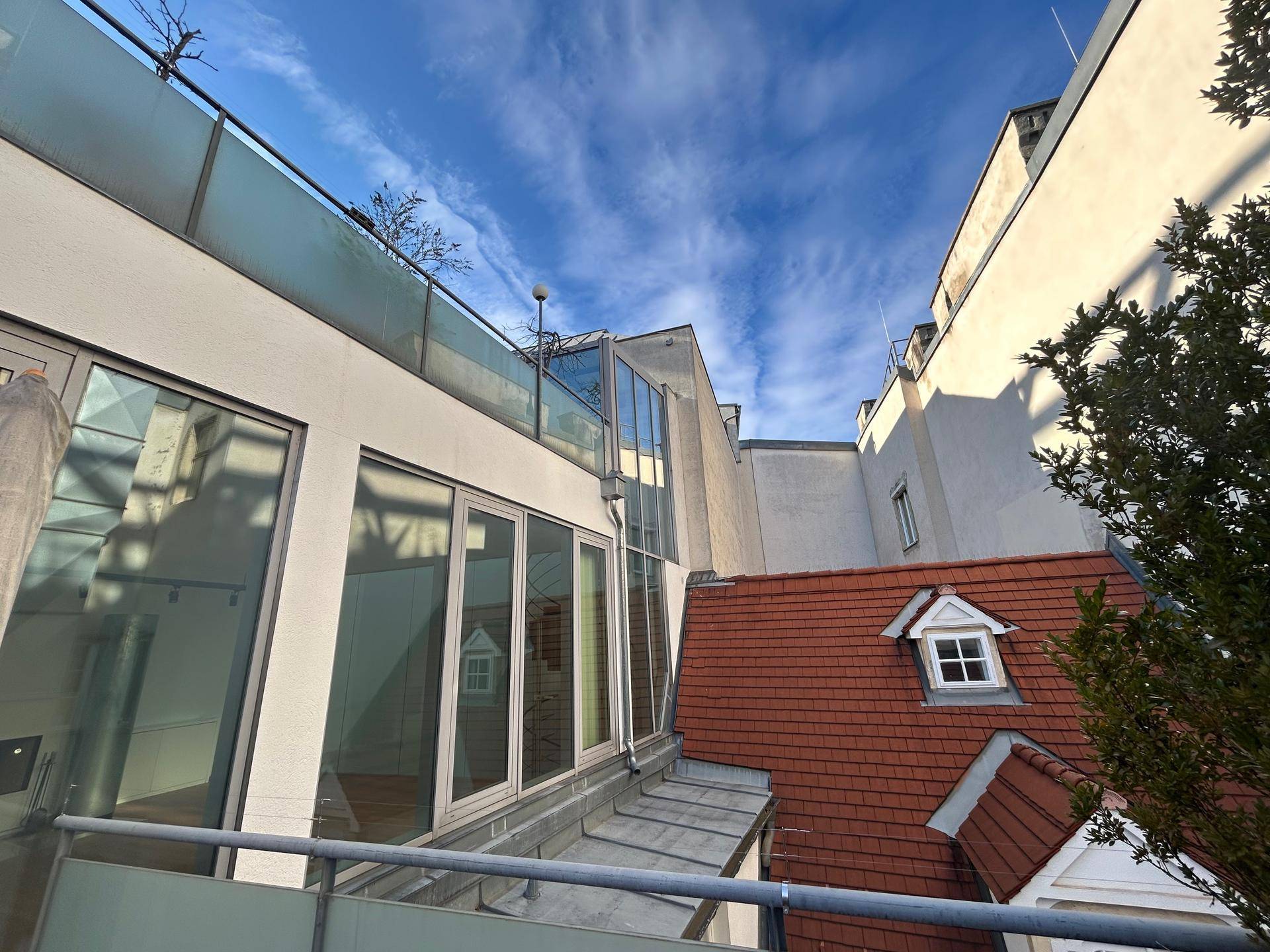 Moderne Architektur mit großen Glasflächen und Dachterrasse neben traditionellen Dächern.