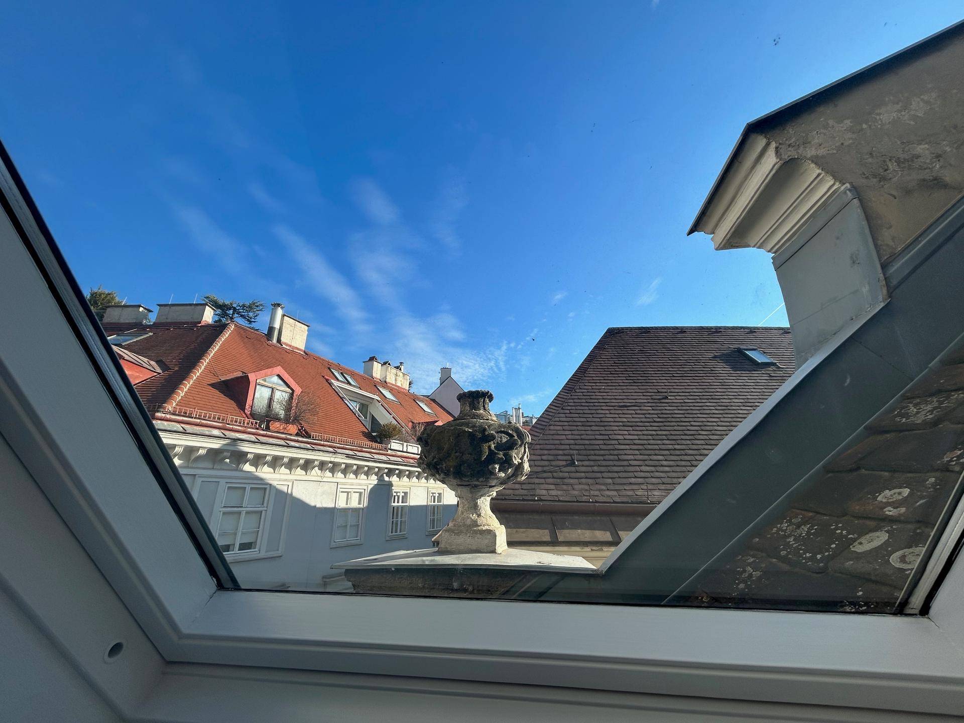 Blauer Himmel über den Dächern der Stadt, gesehen durch ein Dachfenster.