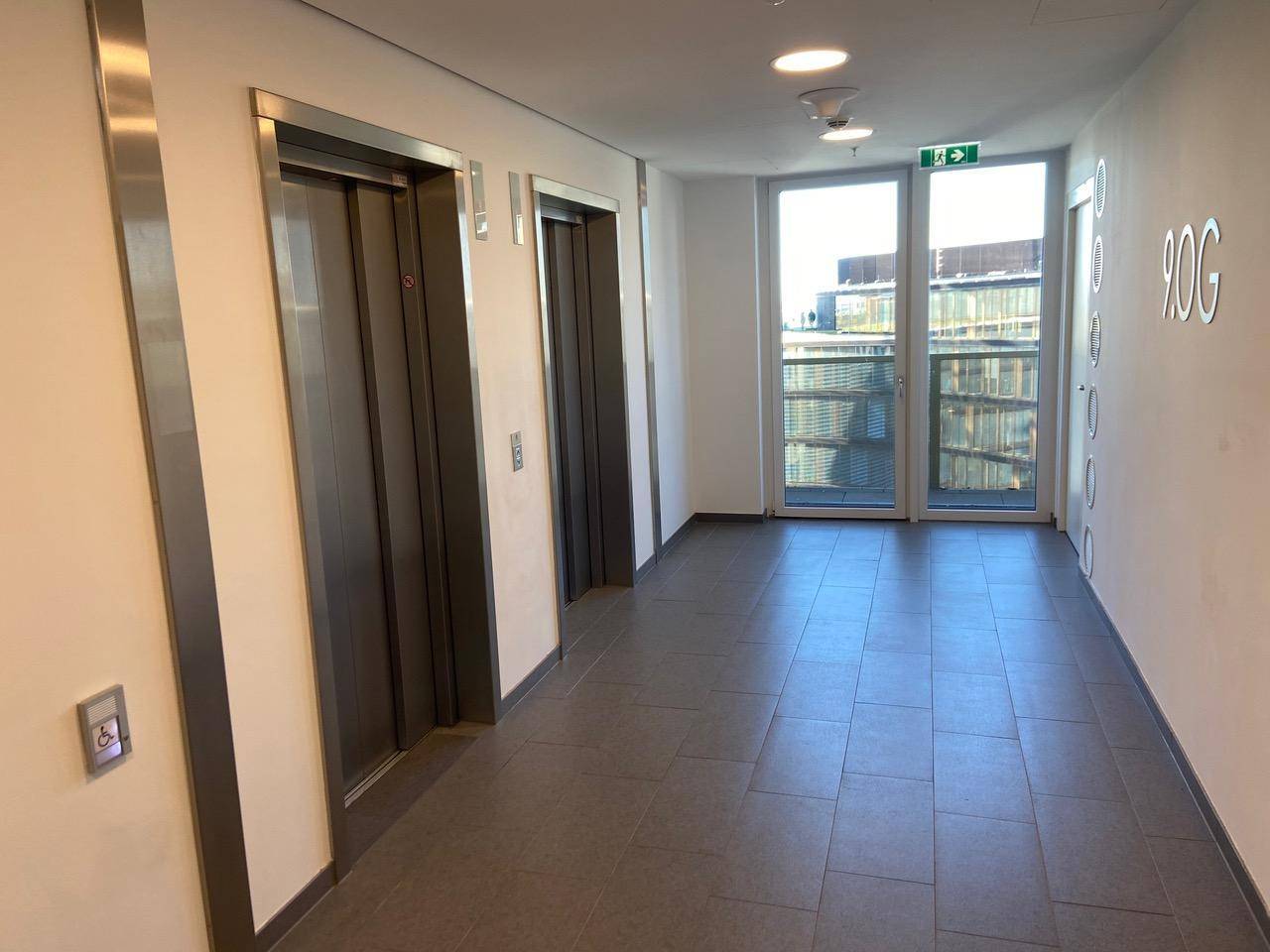 Moderner Flur mit zwei Aufzügen, großen Fenstern und einem Hinweis auf die 9. Etage.