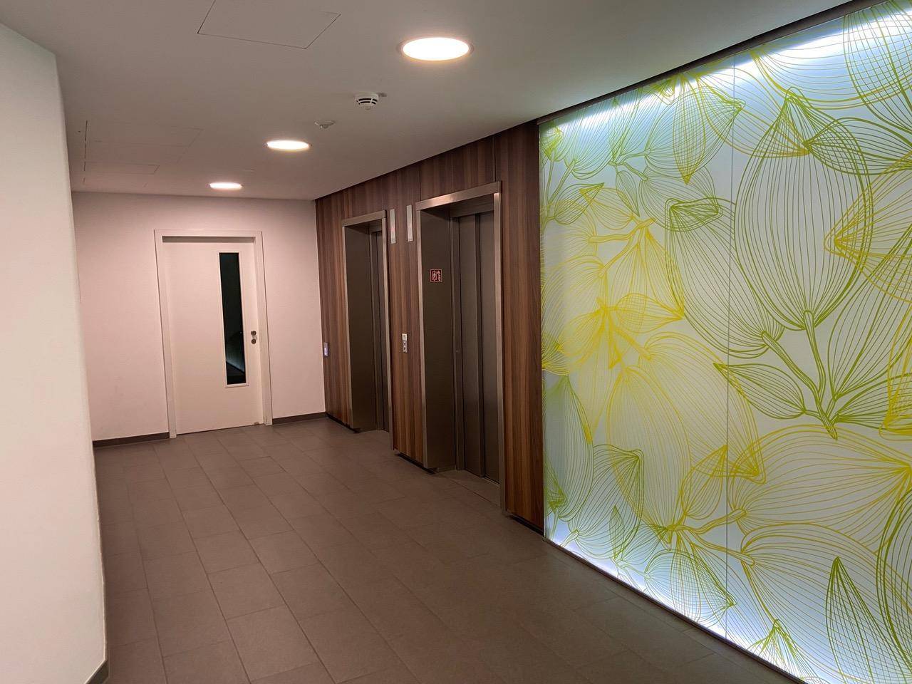 Heller Flur mit zwei Aufzügen und einer dekorativen Wandverkleidung mit floralem Muster.