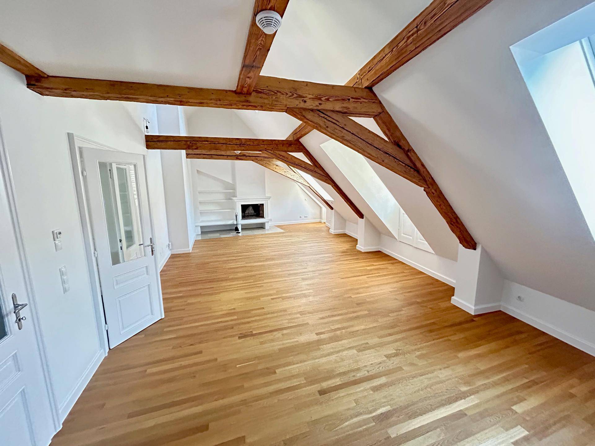 Geräumiges Dachgeschoss mit sichtbaren Holzbalken, Parkettboden und integriertem Kamin.