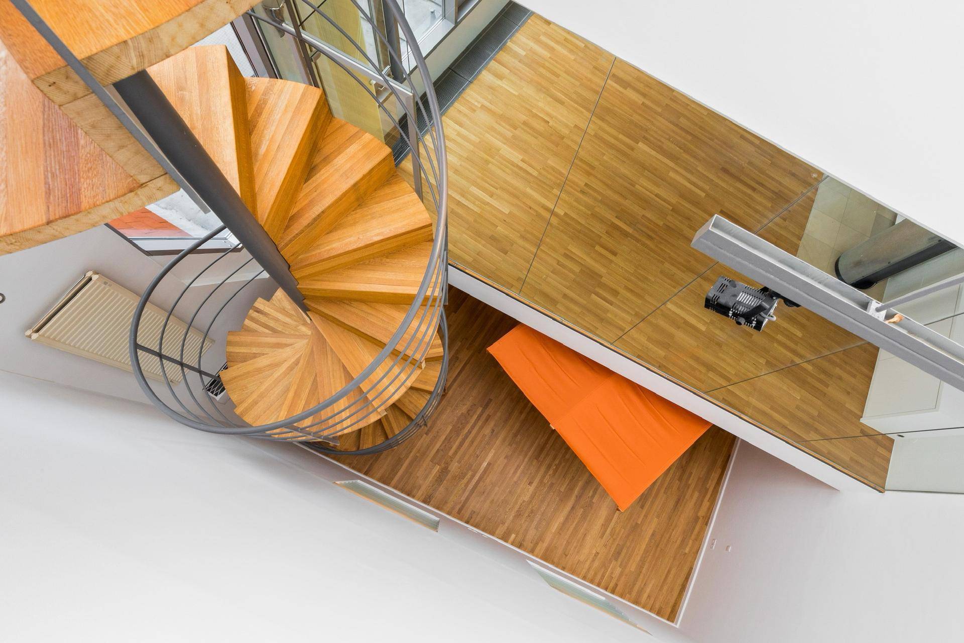 Blick von oben auf die elegante Holz-Wendeltreppe und den Parkettboden.