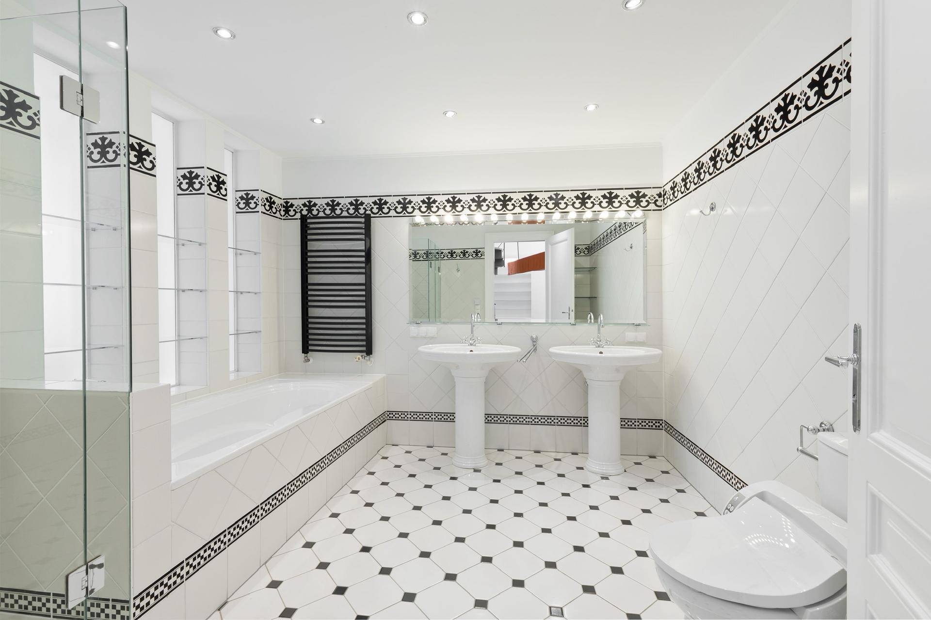 Großes Badezimmer mit Doppelwaschbecken, Badewanne und schwarz-weißen Fliesen.