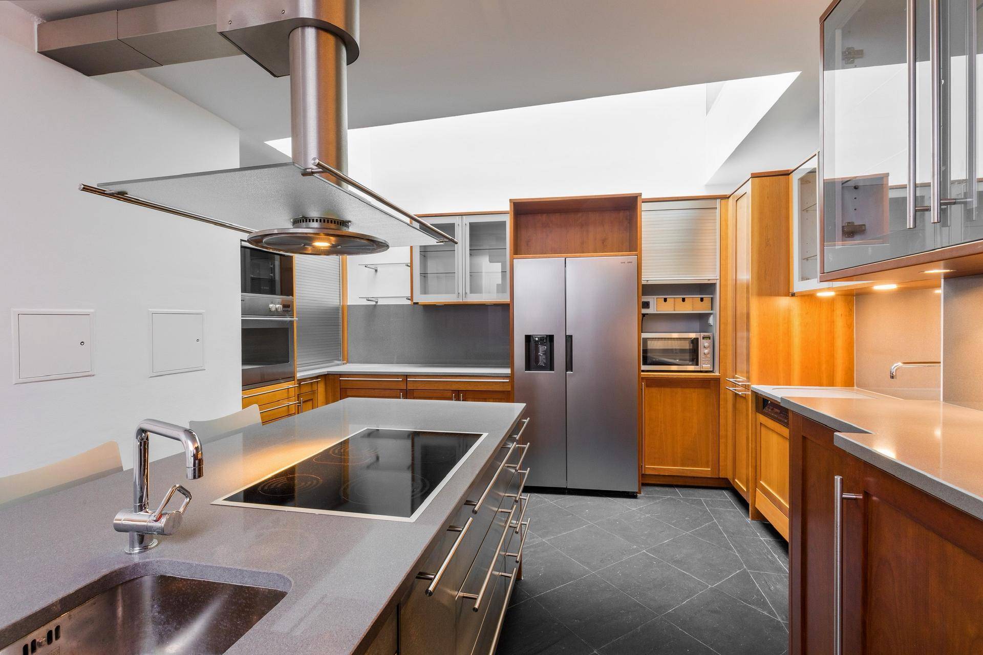 Moderne Küche mit dunklem Fliesenboden, Holzschränken und Kücheninsel mit Induktionskochfeld.