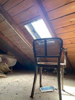 Heller Dachbodenbereich mit Holzbalken, schräger Holzdecke und einem Dachfenster für natürliches Licht.